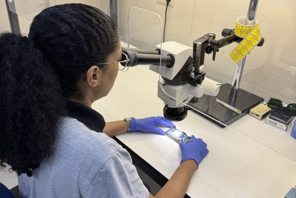 Medewerker controleert een printplaat onder de microscoop in een flow cabinet
